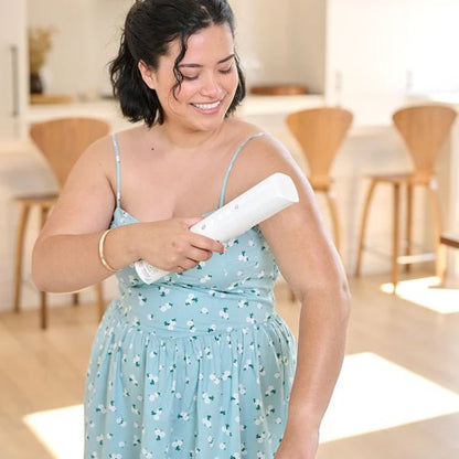Woman in a light blue dress holding self tanner device with glowing skin